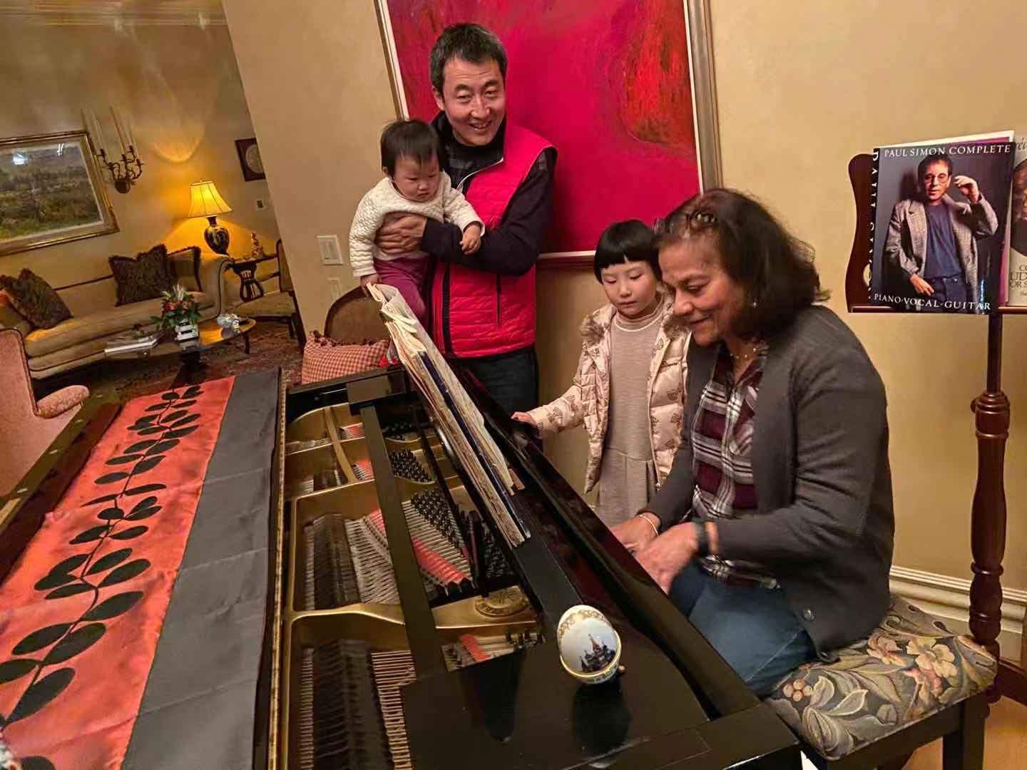 Dr. Wang and his family visiting Prof. D'Souza at her home; Prof. D'Souza teaches piano to his daughter